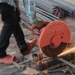 Construction builder worker with grinder machine cutting metal reinforcement rebar rods at building site and unsafe