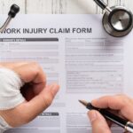 top view man filling up a work injury claim form with stethoscope  medical and insurance concept