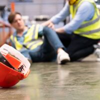 Selective focus at hat, Men worker feel painful and hurt from the accident that happen inside of industrial factory while his co-worker come to give emergency assistance and help. Accident in factory.